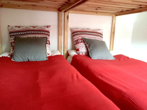Deux lits jumeaux avec literie rouge et coussins aux motifs scandinaves dans la chambre Rouge Canneberge de Couleurs Montagne, Valloire