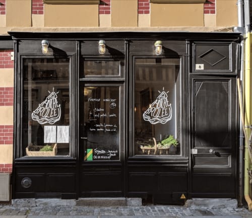 Black storefront of Poulée restaurant in Honfleur, France with neon pear sign and windows