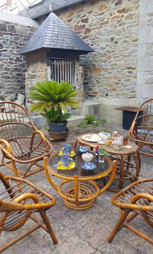 Coin repas extérieur du gîte Les Forges Du Lou avec chaises en rotin, table dressée et architecture en pierre à Jugon-les-Lacs