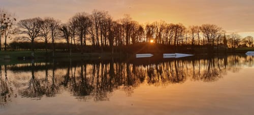 Lever de soleil sur Jugon-les-Lacs avec arbres nus se reflétant dans une eau calme et bateaux amarrés
