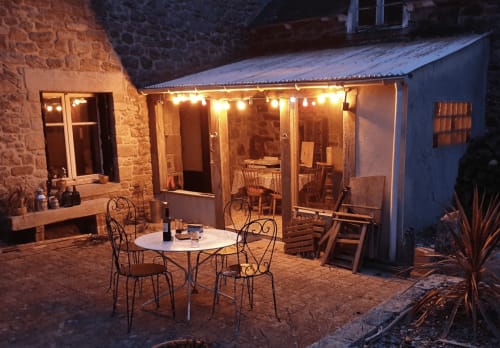 Cour illuminée aux Forges Du Lou B&B à Jugon-les-Lacs avec table dressée et bâtiments en pierre