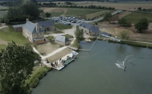 Vue aérienne des Forges Du Lou B&B à Jugon-les-Lacs avec bâtiments en bord de rivière, ponton et parking