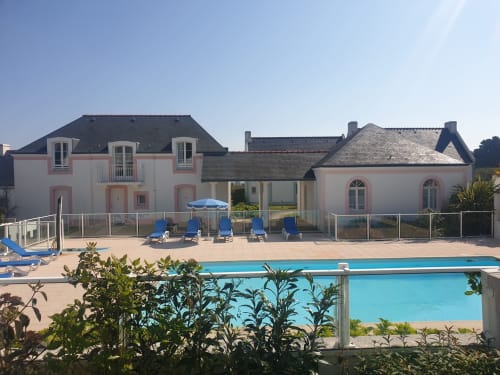 Luxueuse résidence rose et blanche avec piscine, transats bleus et parasol à Locmaria Belle Île en Mer