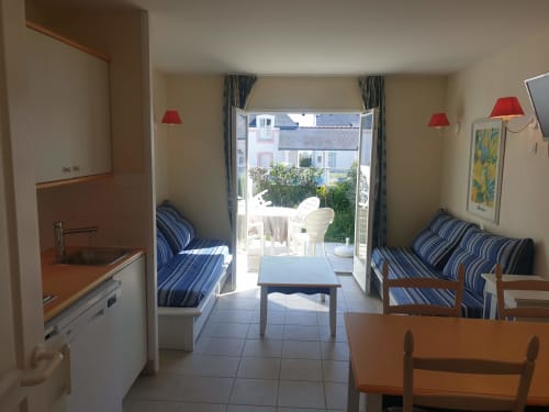 Séjour de l'appartement à Loc'Maria, Belle Île en Mer, avec canapés rayés, terrasse ouverte, kitchenette et appliques murales rouges