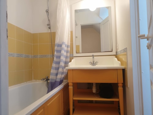 Salle de bain de la Résidence n°82 aux Locations Loc'Maria, Belle Île en Mer avec carrelage jaune, meuble-lavabo en bois, miroir et baignoire