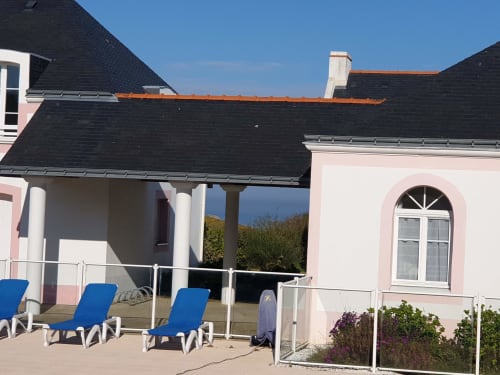 Terrasse d'appartement côtier à Loc'Maria Belle-Île avec transats bleus, pergola couverte et façade villa rose