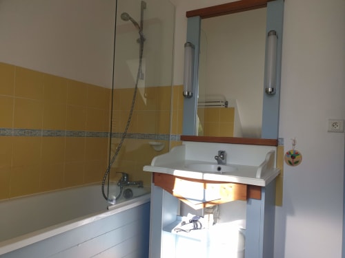 Salle de bain moderne aux murs de carrelage jaune, lavabo blanc, meuble bleu et douche vitrée à la location Belle Île