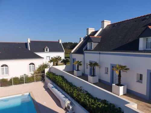Immeubles modernes blancs avec vue sur piscine à Locmaria, Belle Île en Mer, palmiers et toits en ardoise bleue