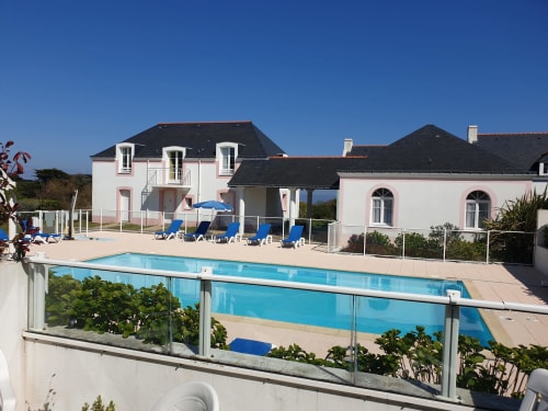 Loc'Maria Belle Île-en-Mer : résidence balnéaire avec piscine chauffée, transats et bâtiment blanc sur la côte française