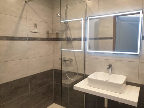 Salle de bain moderne dans un appartement de Belle Île-en-Mer avec douche à l'italienne, vasque de design, meuble miroir et finitions en carrelage foncé