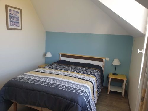 Chambre lumineuse avec mur bleu turquoise, lit en bois, literie à motifs, lampes jumelées et lucarne à Locmaria Belle Île