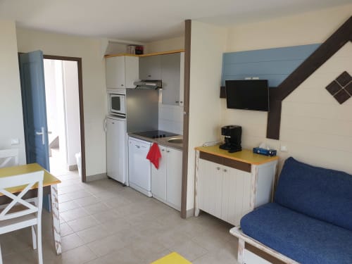 Appartement 103 à Loc'Maria Belle Île en Mer : cuisine, coin repas, canapé et TV dans un espace de vie ouvert