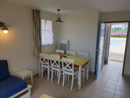 Salle à manger lumineuse avec table jaune et chaises blanches, vue sur la mer par les portes vitrées, location Locmaria