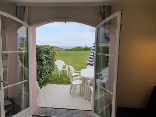 Portes ouvertes sur la terrasse de Belle Île avec chaises blanches, pelouse verdoyante et vue sur mer à l'appartement de Locmaria