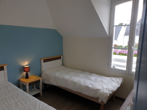 Chambre moderne avec lits jumeaux, mur d'accent bleu canard, portes-fenêtres donnant sur la vue mer à Loc'Maria Belle Île en Mer