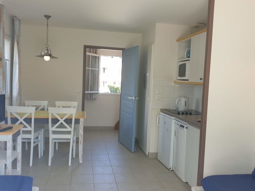 Cuisine moderne et espace repas de l'appartement Loc'Maria Belle Île avec table blanche, chaises bleues et kitchenette compacte