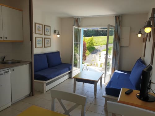 Séjour moderne avec sièges bleus, table à manger, cuisine et portes vitrées donnant sur le jardin à Loc'Maria Belle