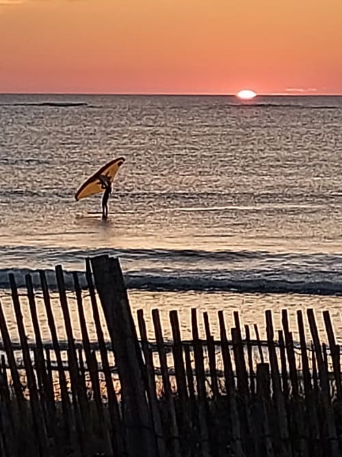 Pratiquant le wing-foil au coucher de soleil, sur les eaux tranquilles près de Ty Coz Breizh, chambres d'hôtes situées à Lorient, Bretagne Sud, créant un spectacle impressionnant de sport et de nature dans un cadre idyllique