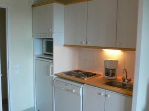 Cuisine compacte avec meubles blancs, plan de travail en bois, cuisinière à gaz et électroménagers en acier inoxydable à l'appartement Loc'Maria
