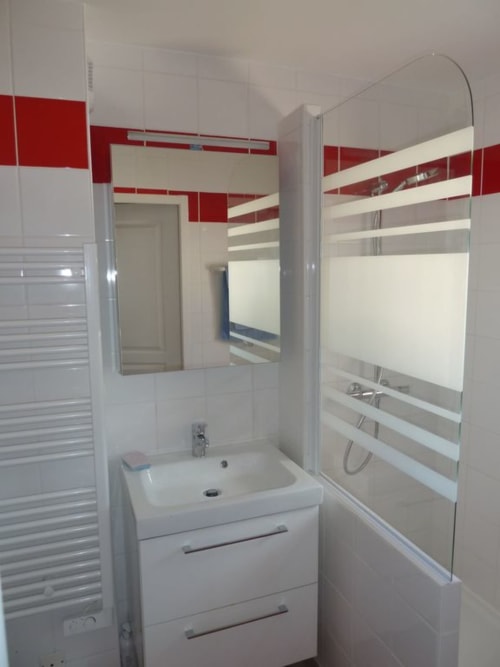 Salle de bains moderne dans un appartement de Belle Île en Mer avec lavabo blanc, carrelage rouge et blanc, et douche vitrée