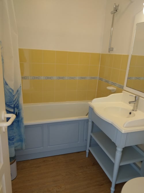 Salle de bain lumineuse dans un appartement de Belle Île en Mer avec carrelage jaune, lavabo blanc et baignoire aux panneaux bleus