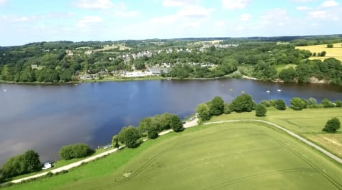Vue aérienne du gîte Les Forges Du Lou au bord du lac de Jugon en Bretagne, entouré de prairies vertes et de forêts