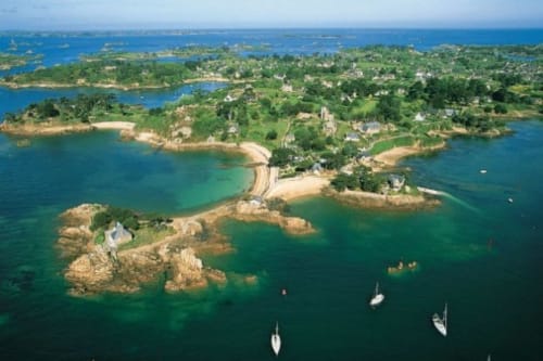 Vue aérienne de Jugon-les-Lacs avec voiliers, plages de sable et forêts verdoyantes entourant une eau turquoise