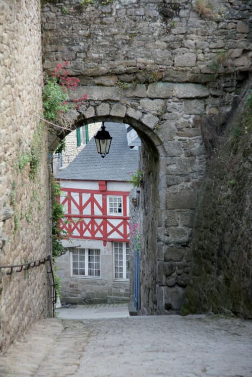Voûte en pierre ouvrant sur un bâtiment à colombages rouges aux Forges Du Lou, Jugon-les-Lacs, France