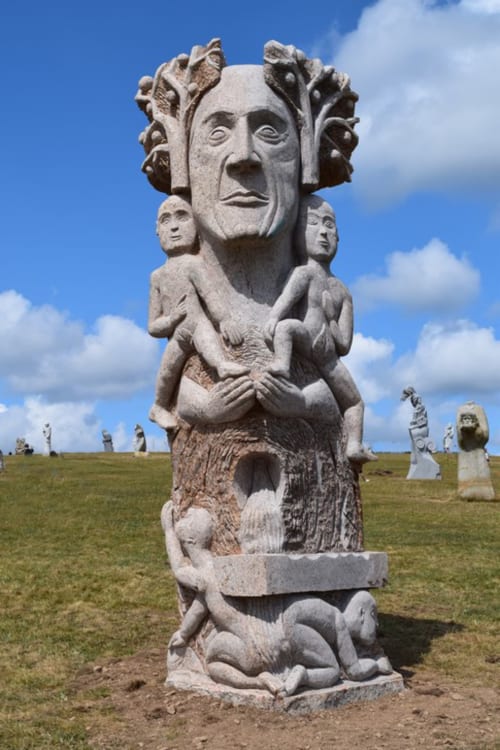 Sculpture de totem en pierre aux Forges Du Lou, Jugon-les-Lacs, avec figures celtiques et ciel bleu
