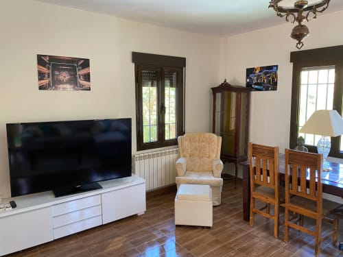 Sala de estar luminosa con TV, sillón beige, sillas de comedor de madera y puertas de cristal en Chalet Dani cerca de Puy Du Fou en Argés