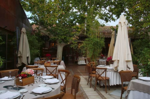 Elegante terraza gastronómica al aire libre en los Chalets Junto A Puy Du Fou con sillas de madera, sombrillas blancas y muros cubiertos de enredaderas