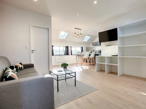 Appartement moderne ouvert à la Résidence L'Hermitière avec coin séjour, cuisine équipée, étagères blanches et vue sur le jardin