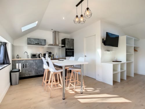 Cuisine et salle à manger ouvertes modernes à la Résidence L'Hermitière avec étagères blanches, mobilier gris et lumière naturelle