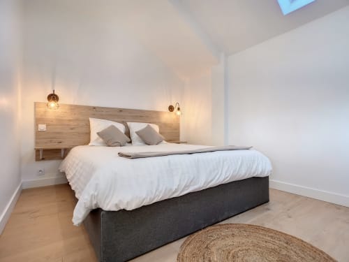 Chambre moderne à la Résidence L'Hermitière avec literie blanche, tête de lit en bois, luminaires suspendus et parquet