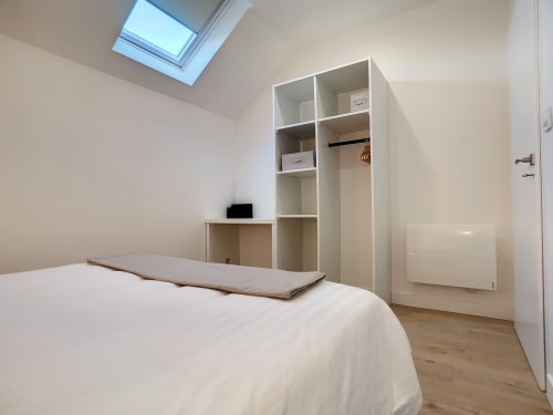 Chambre mansardée lumineuse avec puits de lumière, lit blanc, placard intégré et parquet à la Résidence L'Hermitière, France