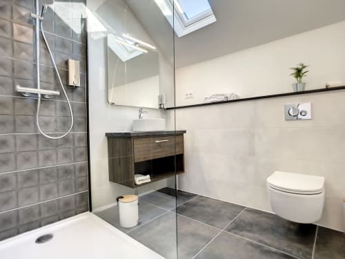 Salle de bains moderne à la Résidence L'Hermitière avec douche à l'italienne, toilettes murales, vasque en bois et puits de lumière