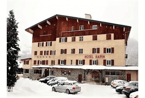 Esterno dell'Hotel Rapin innevato a Valloire, Francia con facciata crema e rossa e auto parcheggiate