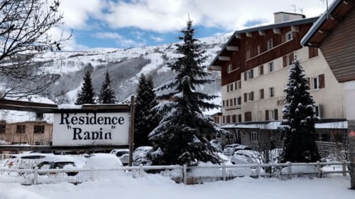 Enseigne de la Résidence Rapin sous la neige à Valloire avec les montagnes alpines et bâtiment hôtelier en arrière-plan