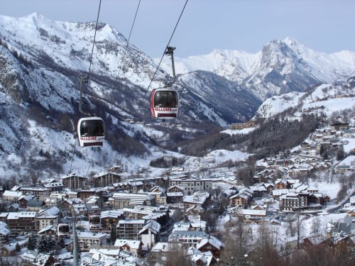 Télécabine de Valloire surplombant un village alpin enneigé avec pics montagneux en Savoie française