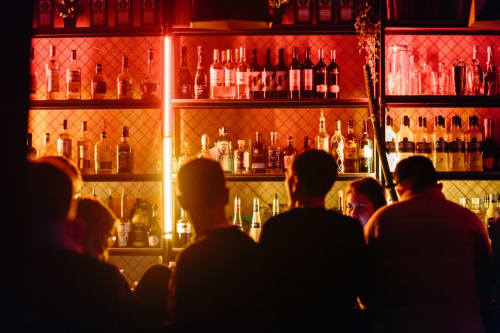 Clients au bar Couleurs Montagne à Valloire admirant les étagères de spiritueux illuminées en rouge avec un éclairage ambiant chaleureux