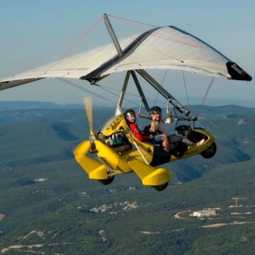 Deux pilotes en deltaplane motorisé jaune vif survolant le paysage forestier de Valloire