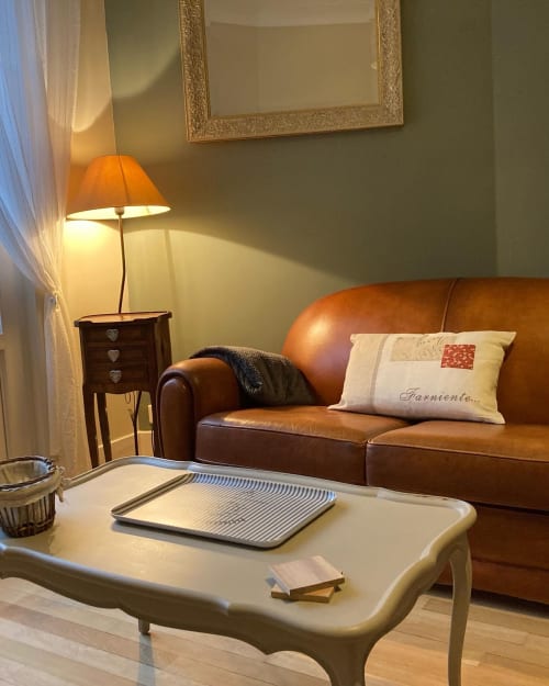 Coin salon douillet de La Maison Virginie avec canapé en cuir marron, table basse blanche élégante et éclairage chaleureux