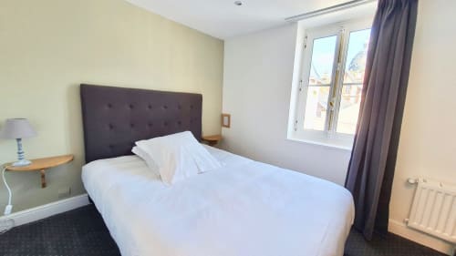Petite chambre d'hôtel aux Cabines à Houlgate avec lit, tête de lit foncée, fenêtre, lampe et radiateur