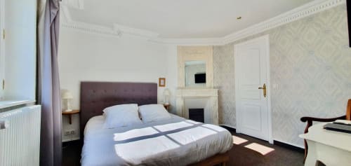 Chambre spacieuse de l'hôtel Les Cabines à Houlgate avec lit à tête de lit violette, cheminée et mobilier moderne
