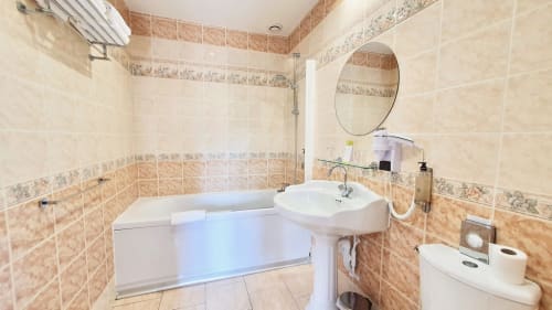 Salle de bain lumineuse de la chambre Les Cabines, Houlgate, avec baignoire, lavabo sur colonne et carrelage beige