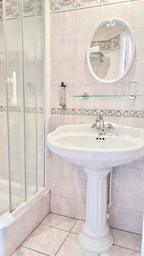 Salle de bains moderne avec lavabo sur colonne, miroir rond blanc, cabine de douche vitrée et carrelage décoratif à l'hôtel Les Cabines