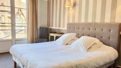 Chambre supérieure aux Cabines à Houlgate avec lit double, tête de lit grise et vue sur la ville depuis la porte du balcon