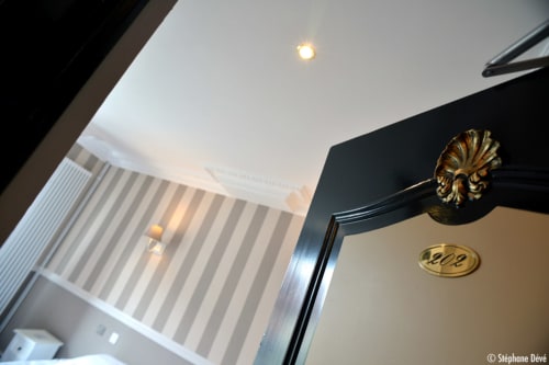 Chambre d'hôtel Les Cabines 2009 à Houlgate avec plafonnier, encadrement de porte noir orné de dorures et papier peint rayé