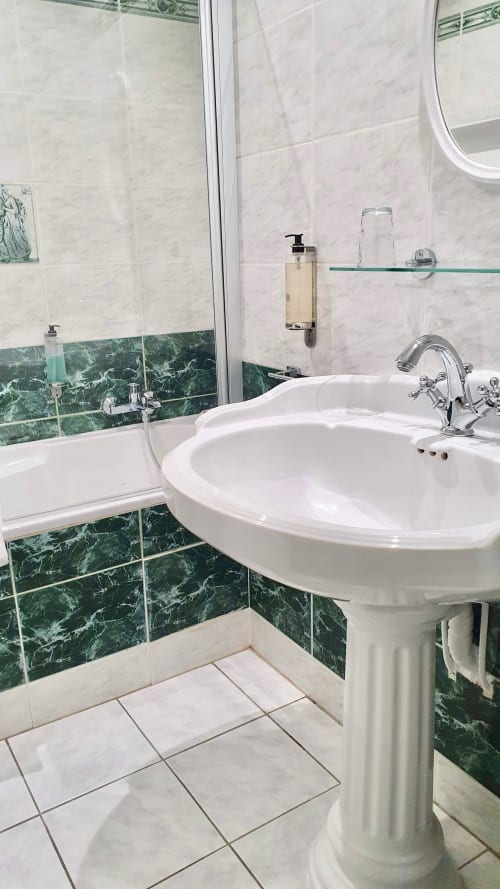 Salle de bains moderne de l'hôtel Les Cabines à Houlgate avec lavabo sur piédestal, carrelage en marbre vert et baignoire avec paroi de douche en verre
