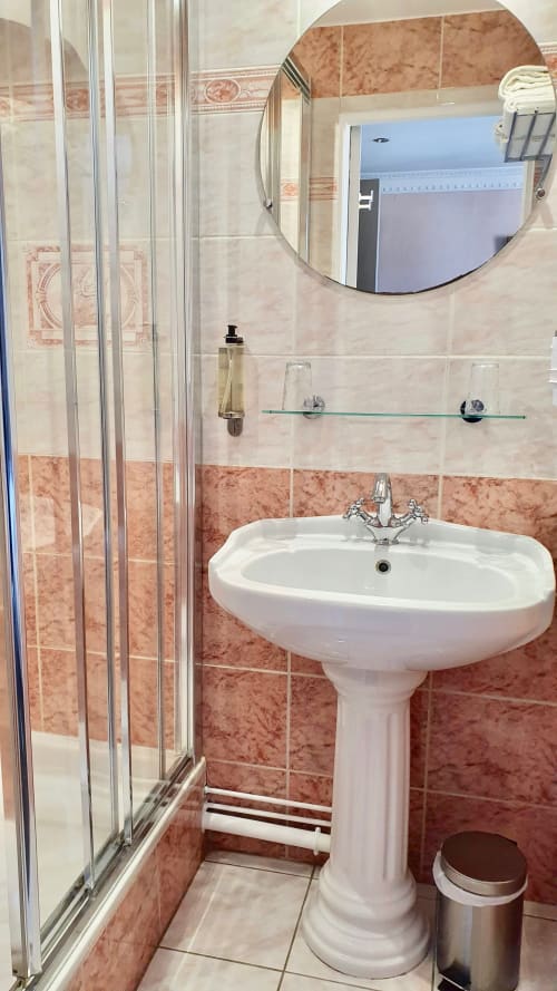 Salle de bains moderne avec lavabo sur piédestal, cabine de douche et miroir rond à l'hôtel Les Cabines à Houlgate